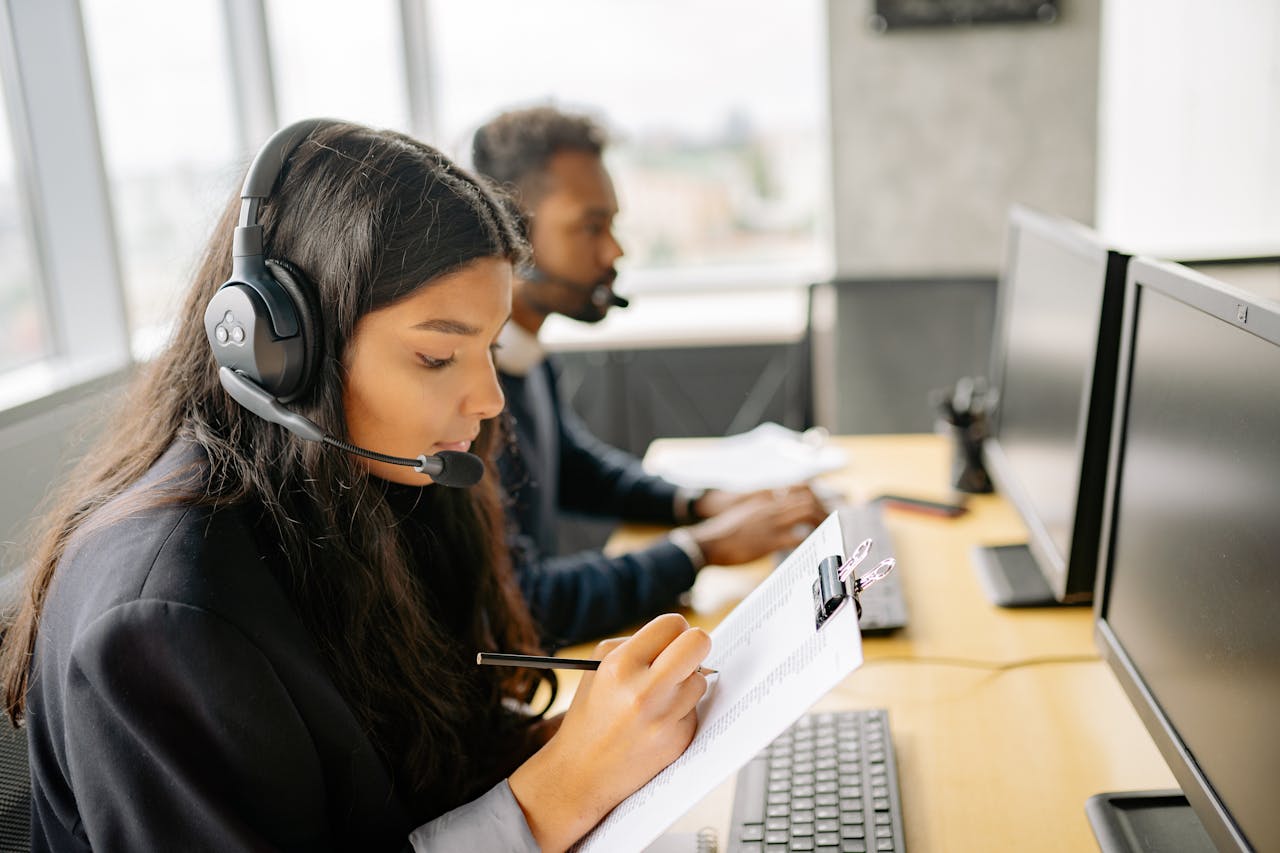 Two call center agents wearing headsets working at desks with computers in a modern office.